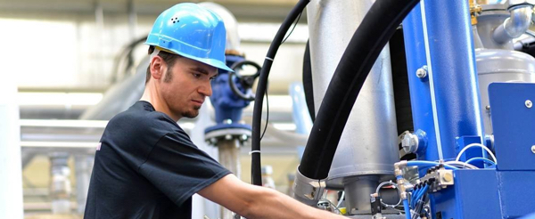 Photo d'un homme portant un casque bleu travaillant sur une machine dans une usine - Illustration société Vulcanic